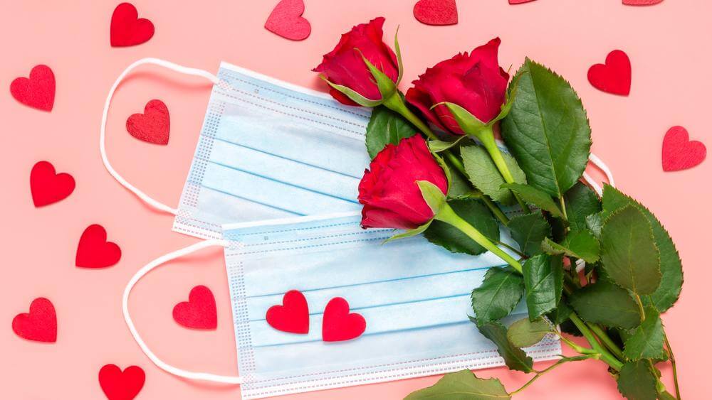 two medical masks, roses and heart-shaped petals on pink background