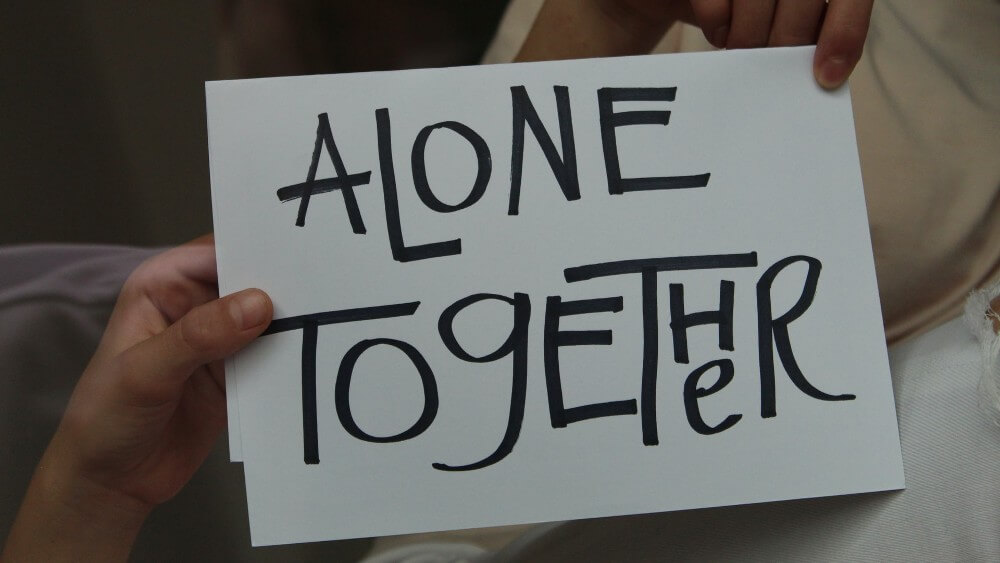 Hand holding a white paper with the inscription "ALONE TOGETHER"