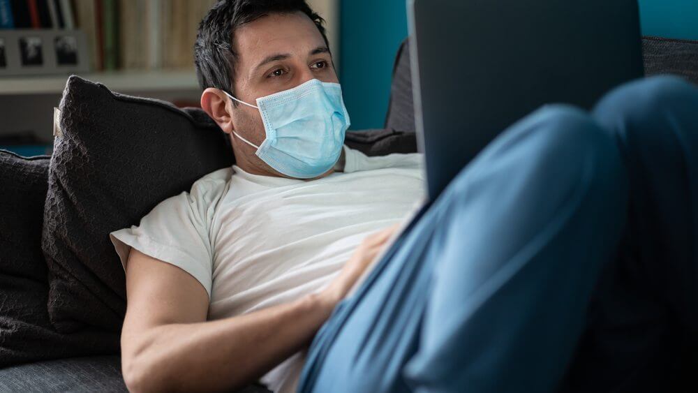 man wearing mask and lying on his sofa calling via a laptop