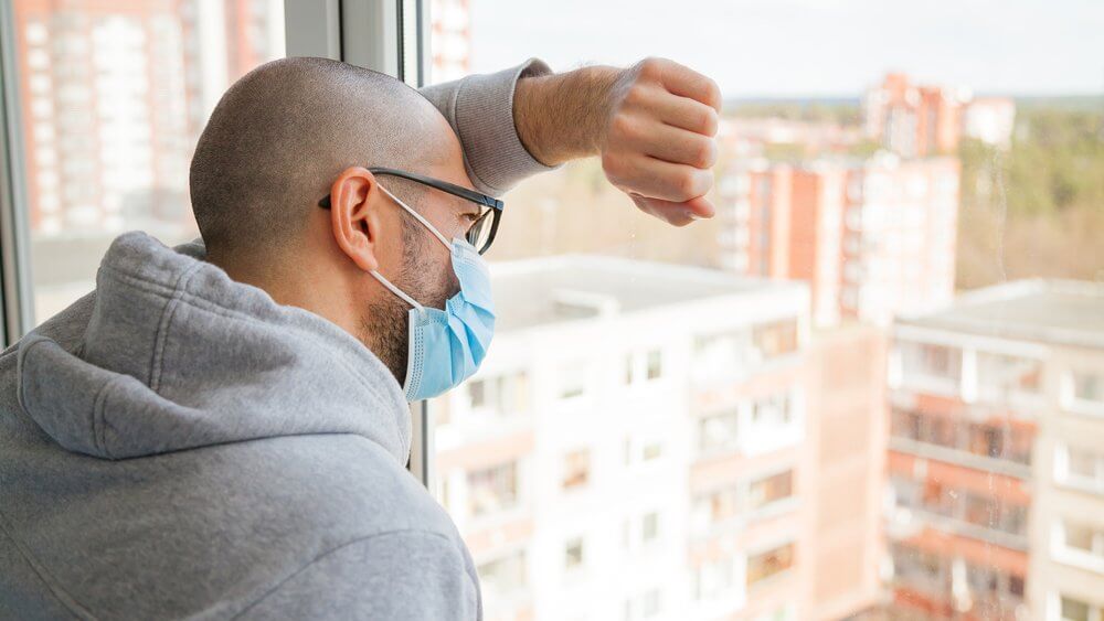 lonely man wearing a face mask looking through a window