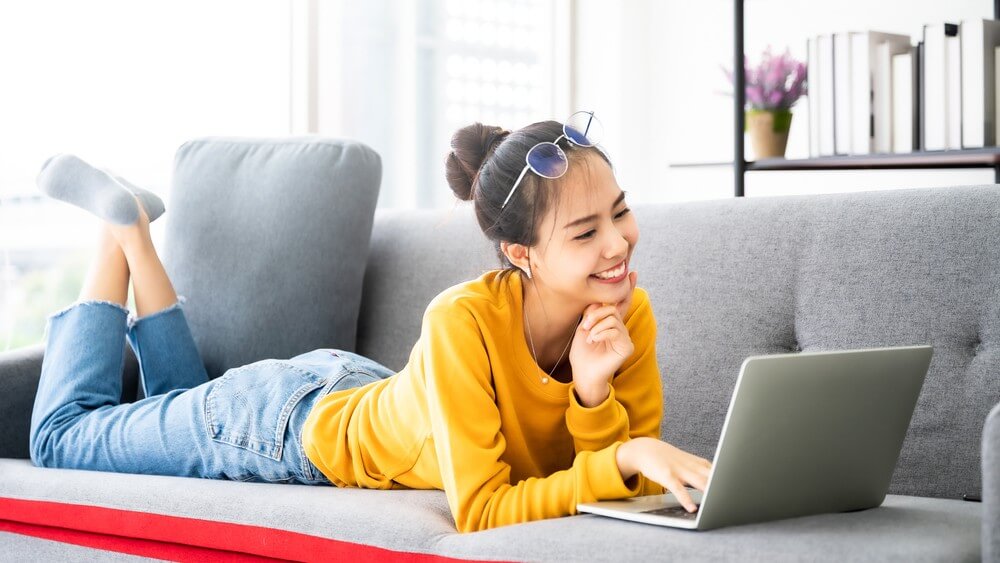 young Asian girl lying on her couch smile on a video chat