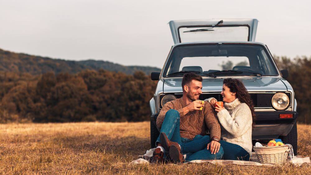 beautiful young couple having a picnic by their car