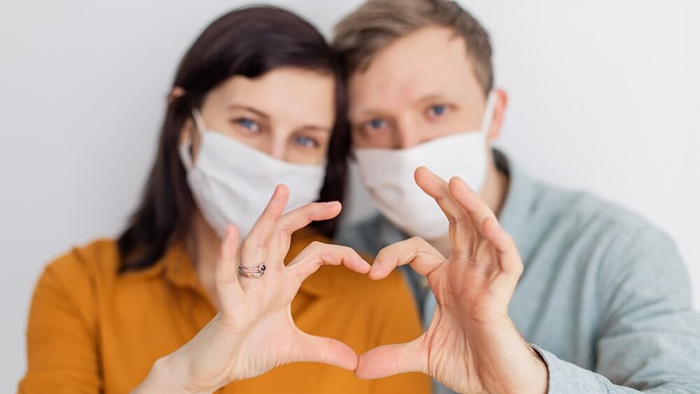 couple wearing white masks making a heart symbol with hands