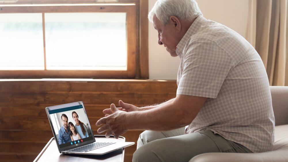 Elderly man video chatting with his son's family vis a laptop