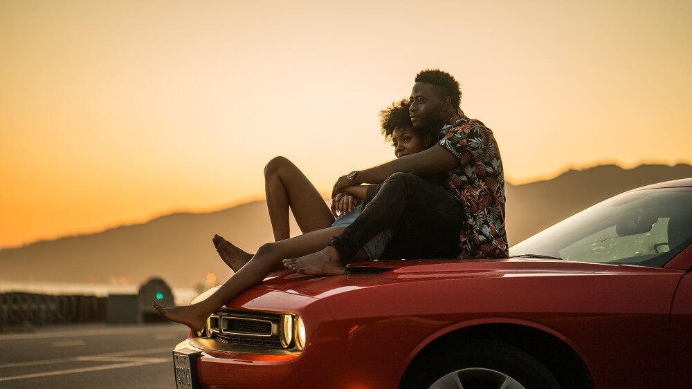 black young couple sitting on a red car at sunset