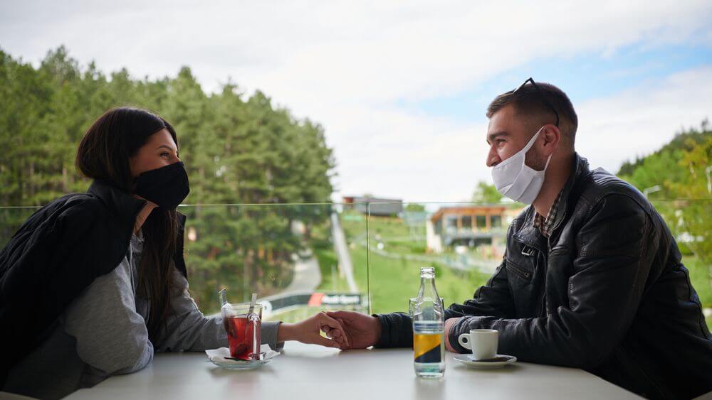 couple on a date wearing masks and holding hands across the table