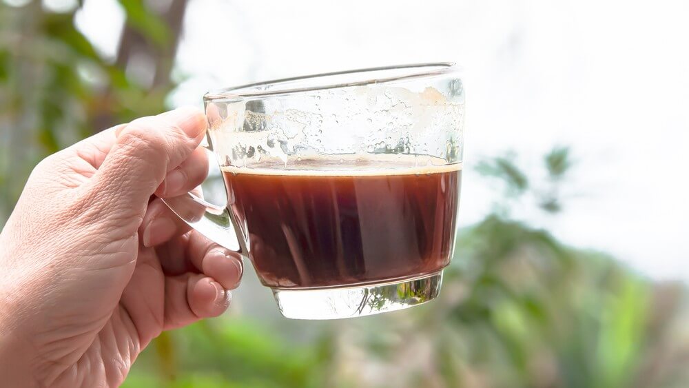 hand holding a glass mug of home brewed coffee