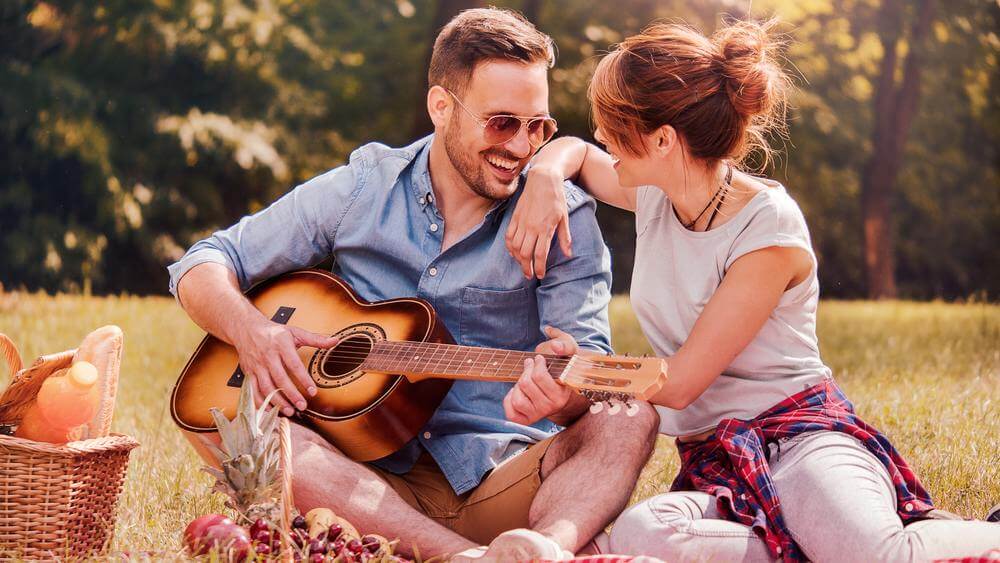 lovely couple enjoying a nice picnic with playing a guitar