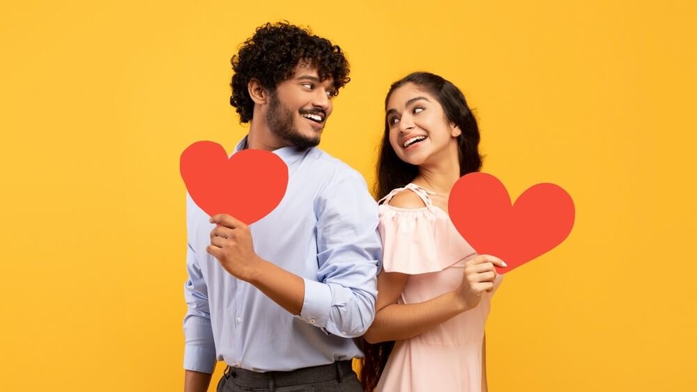 young Indian couple holding paper hearts on yellow background