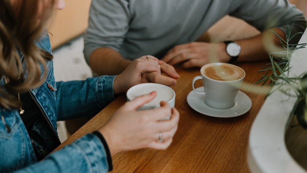 couple holding hands while having coffee