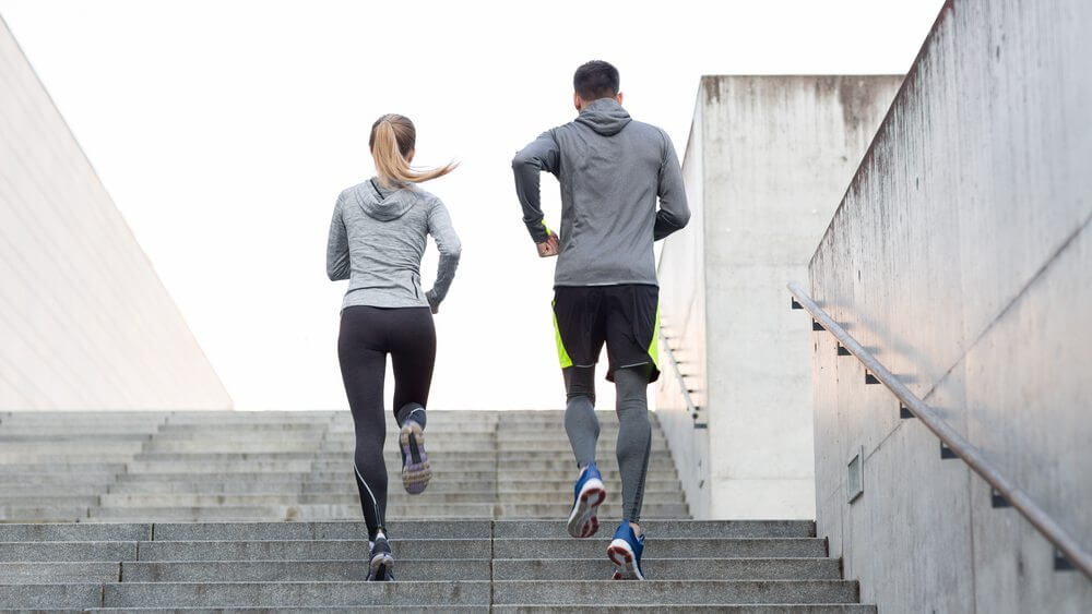 back view of man and woman jogging up the stairs of a stadium together