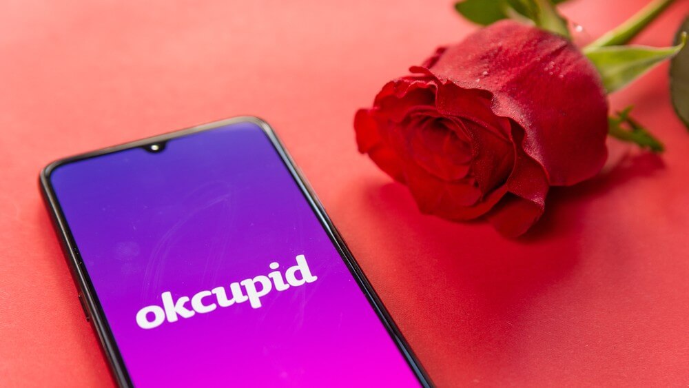 Phone with OkCupid on screen and a rose on red background