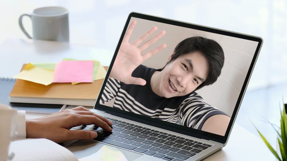 Asian man waving his hand from the other end of a video call