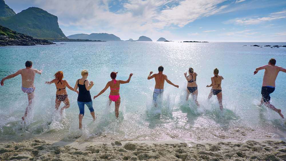 group of friends running into the ocean waves happily