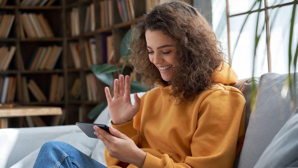 Happy young Hispanic female making a video call and waiving at her phone 