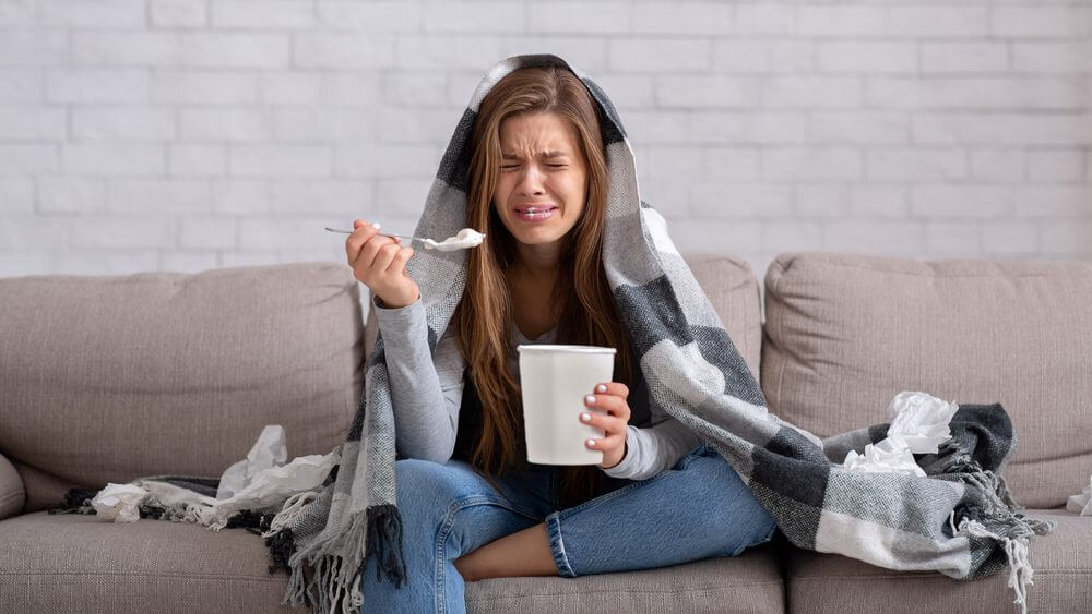 heartbroken woman eating ice cream from a bucket on her sofa