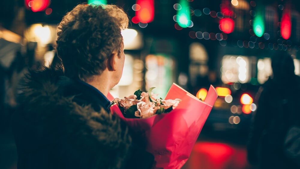 young man holding a bouquet of flowers staring at distant lights 