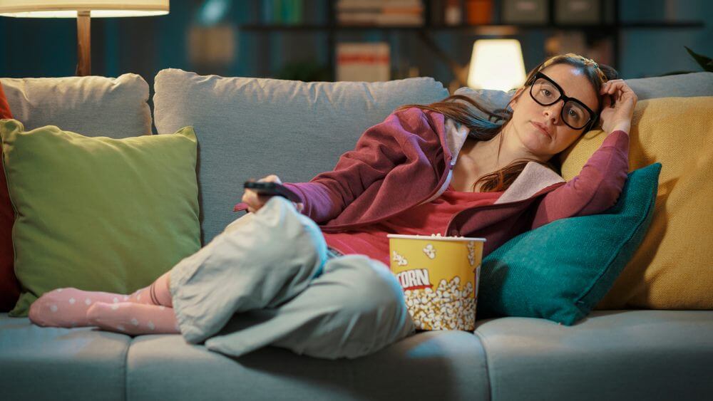 woman lying on the sofa with a bucket of popcorn binging a TV series