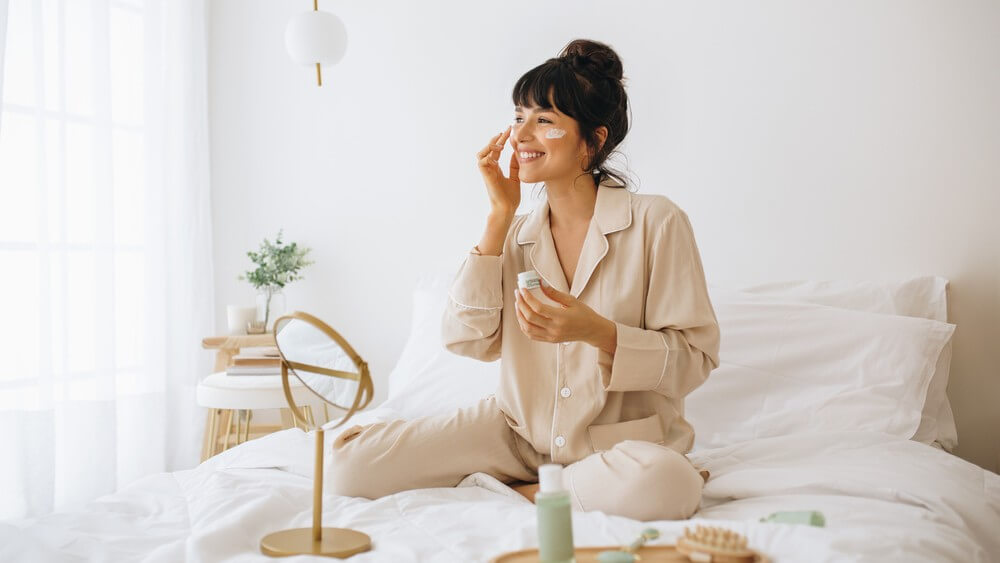 woman doing her routine skincare in bed