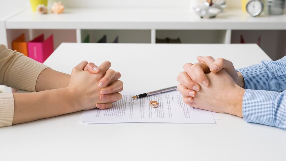 couple sitting across each other on a table with their rings and hands-on the divorce document