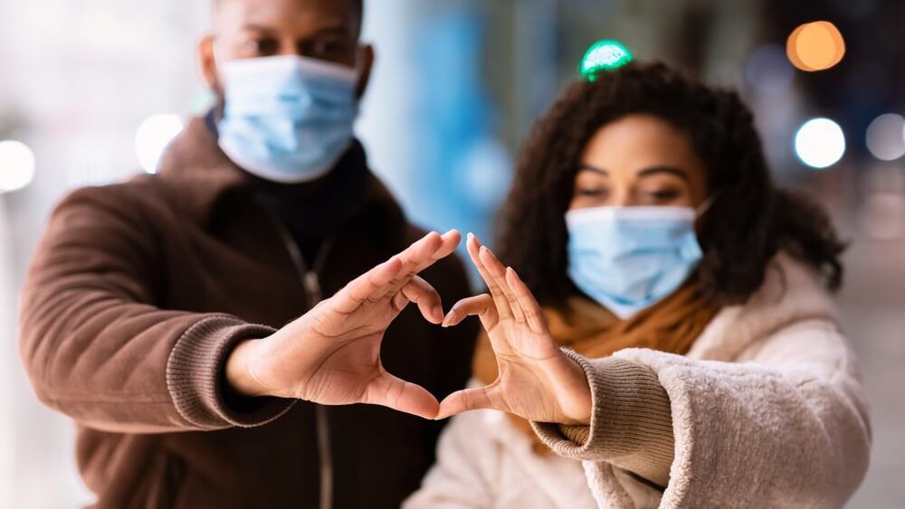 couple wearing face masks during covid-19 making a heart symbol with their hands 