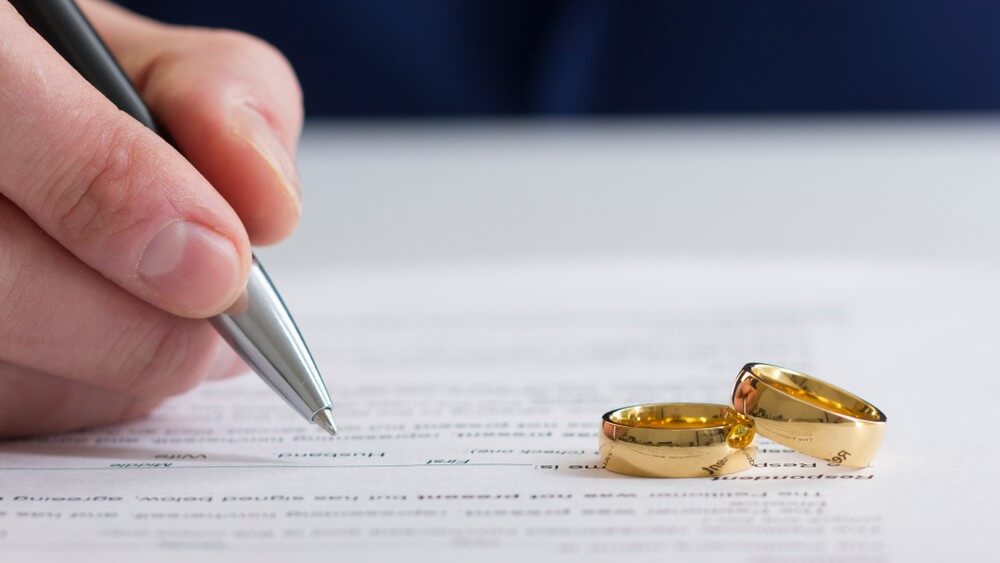 hand of wife signing divorce papers with two rings on it