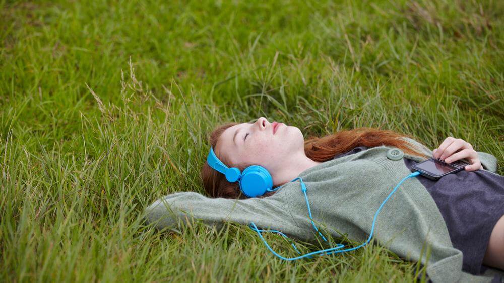 teenage girl listening to headphones while lying on the grass