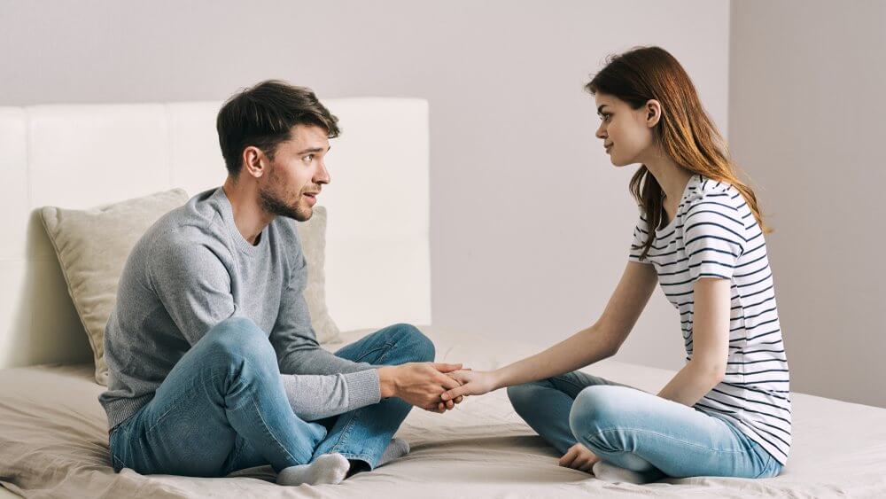 man holding woman's hand while communicating in bed