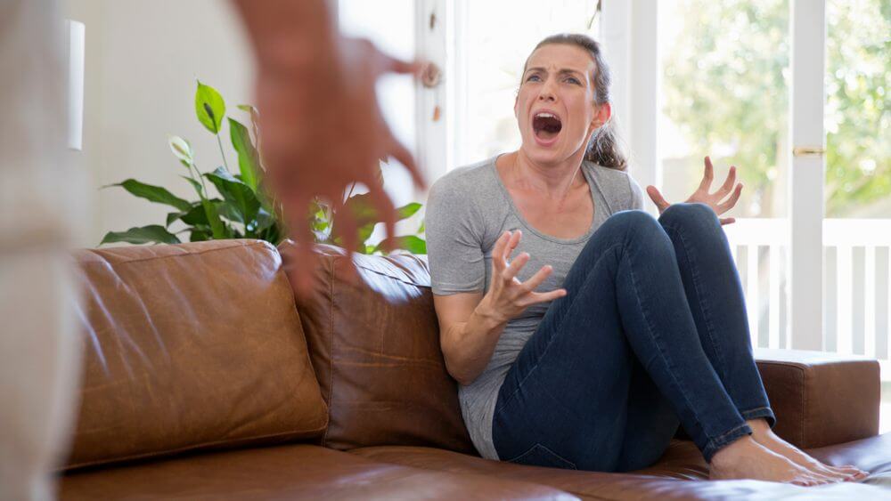 woman sitting on a brown leather sofa screaming at her partner