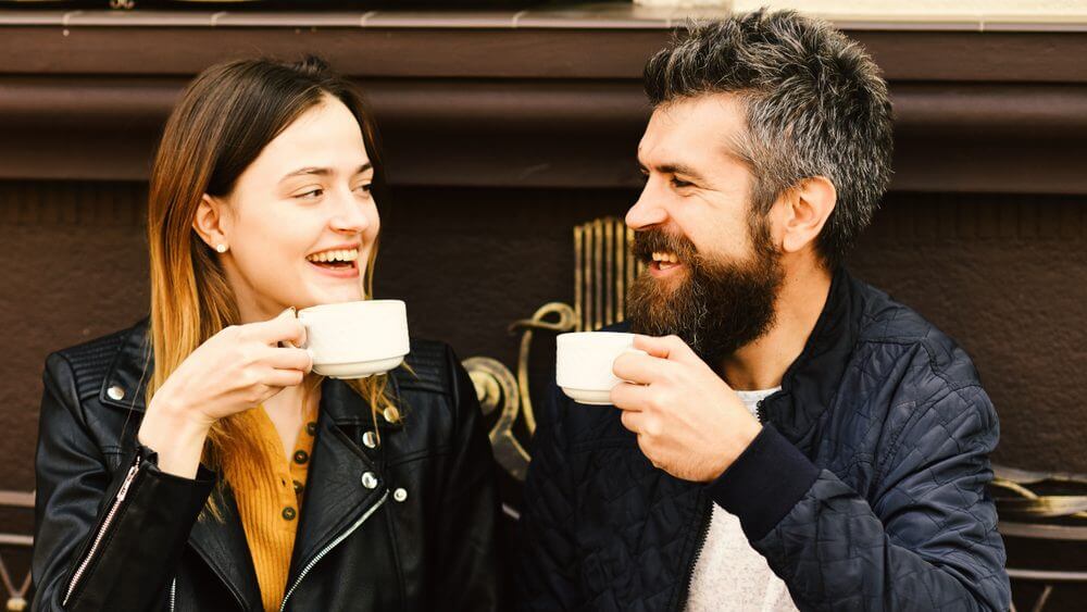 a happy couple in black jackets holding coffee cups, smiling at each other